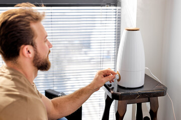 Smart air humidifier emitting water vapor on table, bearded man use turn on modern device, living in smart house. Modern technologies concept. Copy space - obrazy, fototapety, plakaty