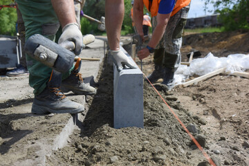 Close-up of a worker banging a hammer on a curb set in cement along the road.