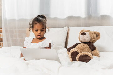 amazed african american child watching movie on laptop near soft toy