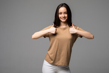 Young woman with thumbs up on gray background