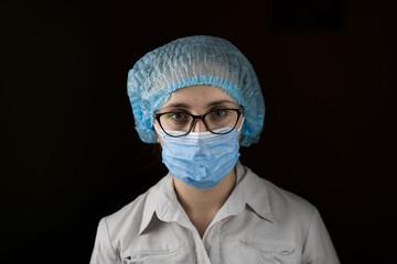 Portrait of a young female doctor in a white coat and mask. Smiling at the camera
