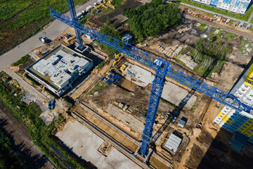 Fototapeta premium Aerial view of construction site crane operating arm jib and tower cranes over building site with concrete foundation