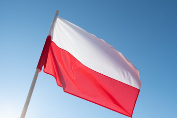 Polish flag waving in wind and sunlight. Flag of Poland on blue sky background. Empty copy space...