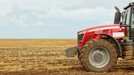 Obraz premium A tractor in a field against the blue sky. A close photo of a modern red tractor.