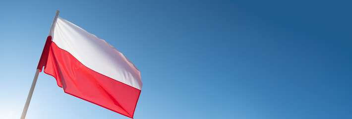 Polish flag waving in wind and sunlight. Flag of Poland on blue sky background. Empty copy space for text.