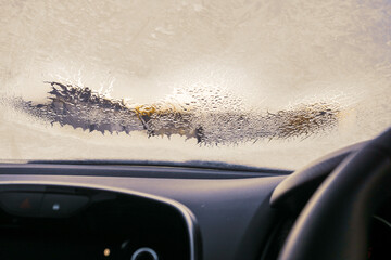 Frosted car windshield with patches of defrosted area. Winter cold season concept. Getting ready to...
