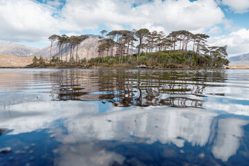 Twelve pines island on Lake Derryclare Lough in Connemara, county Galway, Ireland. Irish nature landscape. Beautiful scene with water, mountains and blue cloudy sky. Nobody. Popular tourist landmark