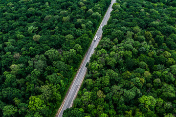 trucks carrying goods on the highway. white truck driving on asphalt road through a green forest. Drone top view seen from the air. Aerial view landscape. drone photography. cargo delivery.