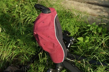 red black cap made of fabric hangs on the handlebars of a sports bike in the green grass and...