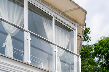 Fototapeta premium View of terrace with full-height windows from floor to ceiling, white curtains and canopy with trees in background