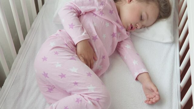 close up authentic cute caucasian little preschool child girl sleep sweetly in white crib on pajama in bedroom during lunchtime. kid is rest lie in bed near window. Childhood, medicine, health concept