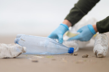 Environmental problem - environmental pollution. There are plastic bottles lying on the beach, which a volunteer removes. Waste recycling. Culture of behavior. Close-up.