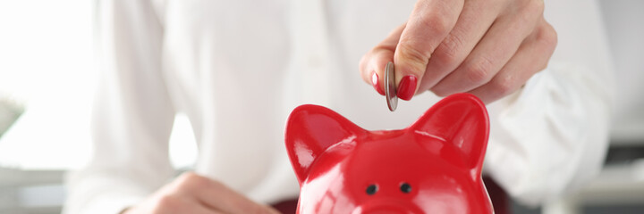 Woman throws coin into piggy bank closeup