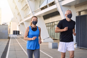 Sportive mature couple wearing protective face masks jogging together in urban environment