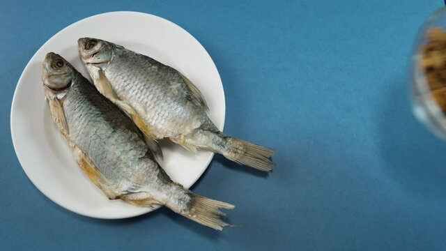 A man's hand in a white glove places a white plate with two dried fish (roach) on the table. Then he puts a transparent bowl of croutons on the table. This is a great beer snack.