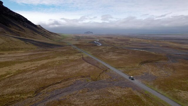 Drone shot following vehicle in Iceland in epic landscape on a gravel road. Mountains and rivers, shot in summer.