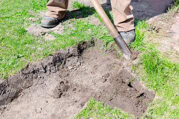 Close-up worker man legs digging soil, ground, details pieces of green fresh lawn grass at city...