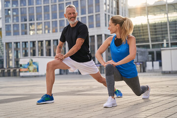 Active sporty middle aged couple, man and woman stretching legs, preparing for running together in...