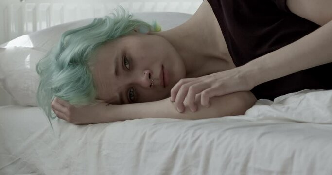 Lonely caucasian woman lying on bed at home. thoughtful sad woman hiding from world. Stress concept. Self harm, swallow pills. Female with short green hair suffering from depression, crying