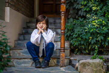 child dressed for holy communion sitting on a ladder in front of his house