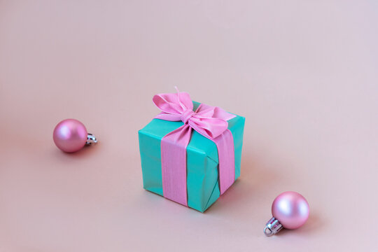 Teal blue gift box with pink bow and Christmas balls on beige background