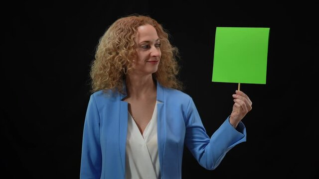 Portrait of smiling woman looking at camera shaking head yes holding green mockup sign in hand. Confident positive Caucasian lady approving endorsing at black background