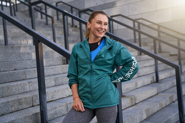 Happy middle aged sportswoman in sportswear smiling away standing outdoors after morning workout in the city