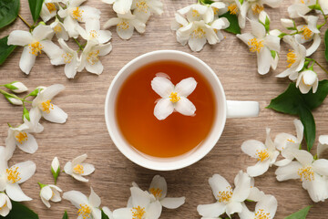 Obraz na płótnie Canvas Cup of aromatic jasmine tea and fresh flowers on wooden table, flat lay
