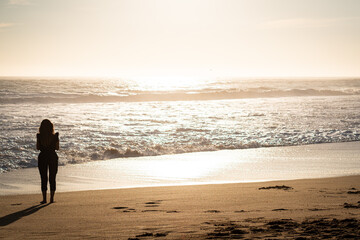 Naklejka premium Silhouette of a young woman contemplating the sunset on the beach