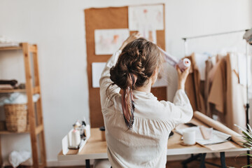 Stylish woman holds thread to create new clothes. Dark-haired lady with ponytaill works on new...