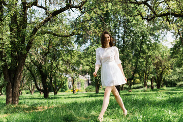 Cheerful woman in summer dress walking on grass in park