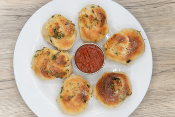 Overhead view of side dish appetizer of garlic flavored bread rolls on a plate served with marinara dipping sauce