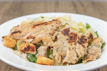 Large grilled chicken breast cut up and topping this very hearty caesar salad in a bowl