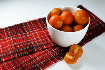 Cherry tomatos' bowl with sliced fruit on a tablecloth.