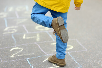 Little boy's legs and hopscotch drawn on asphalt. Child playing hopscotch game on playground on...