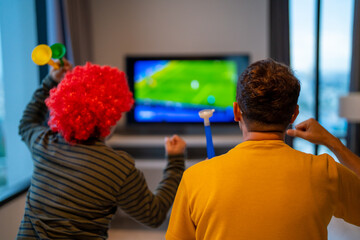 Group of Asian people friends sit on sofa watching and cheering sports games competition on TV together at home. Excited man and woman sport fans celebrate sport team victory in national sports match