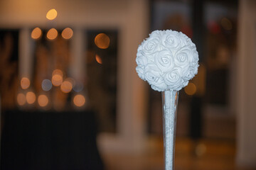 White round faux flower in glass cylinder vase centerpiece at wedding reception table setting with...