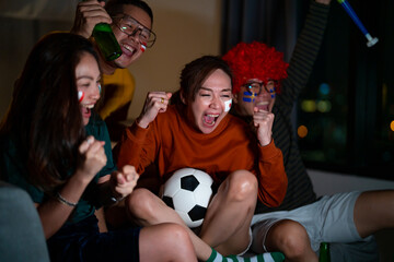 Group of Asian people friends sit on sofa watching and cheering sports games competition on TV...