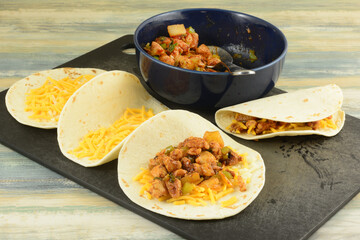 Making BBQ chicken pineapple quesadillas by filling tortillas with shredded cheese and cooked filling on cutting board