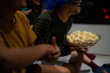 Group of Asian people friends sit on sofa watching and cheering sports games competition on TV...