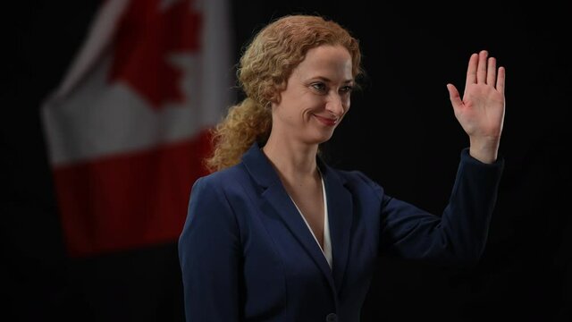 Canadian politician woman smiling waving looking away at black background with national flag. Confident diplomat posing greeting audience at public event