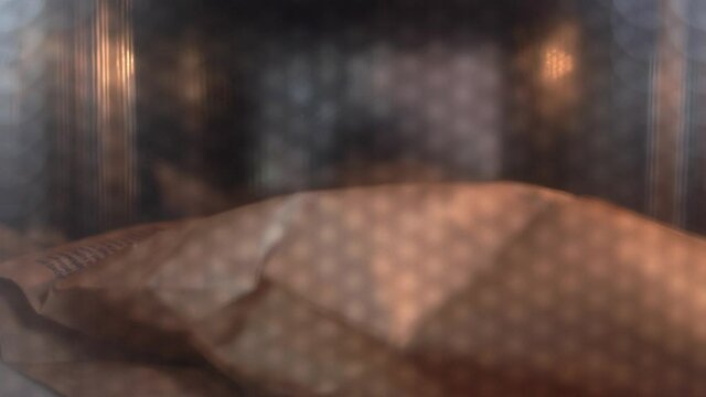 Cooking of delicious popcorn in brown paper bag in contemporary microwave oven view through transparent door extreme closeup
