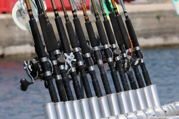 Fishing rods in holders on fishing charter boat parked at harbour on bright sunny day
