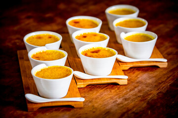 Creme brulee in white ramekins lined with white spoons on rustic background with shallow depth of...