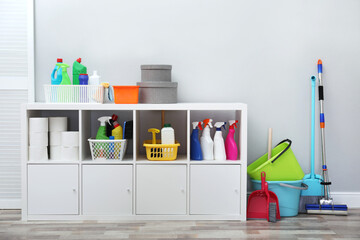 Shelving unit with detergents and cleaning tools near light grey wall indoors