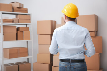 Young man near cardboard boxes at warehouse, back view