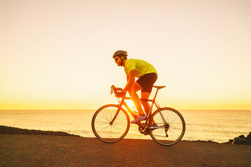 Triathlon competition man cyclist triathlete riding road bike cycling uphill in difficult race during sunset on ocean coast landscape. Fitness active lifestyle.