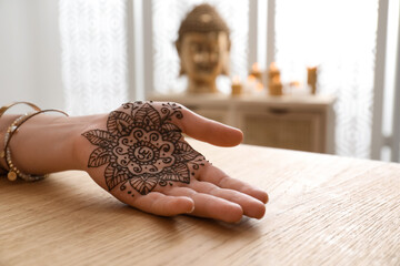 Woman with henna tattoo on palm at table indoors, closeup. Traditional mehndi ornament