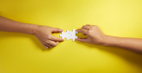 Two hand joining two matching puzzle pieces together in a conceptual image of teamwork and...