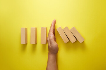Top view of male hand stopping falling dominos on yellow background